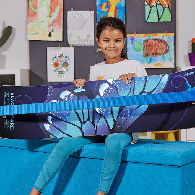 Child holding a Butterfly SlackBoard in a room with artwork on the wall.