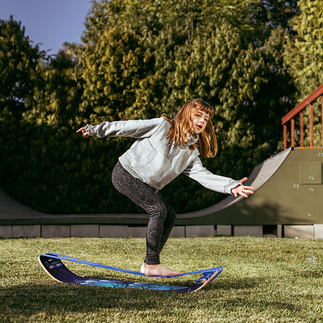 Kid balancing on Butterrfly SlackBoard on grass with trees in the background