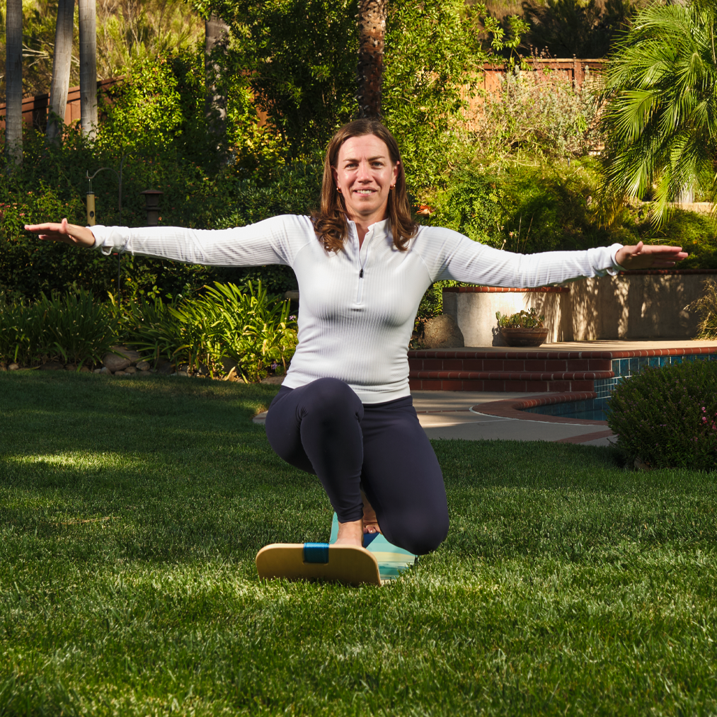 Woman practicing yoga with a slackboard on a grassy lawn with a pool and garden in the background