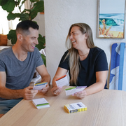 Two people sitting at a table with a deck of GIBBON SlackBoard Exercise cards, smiling and engaged in a conversation.