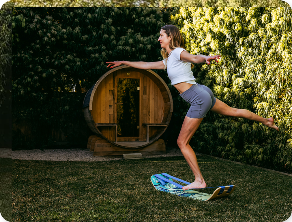 Woman balancong on a waves slackboard plus in a garden with a wooden sauna and greenery in the background