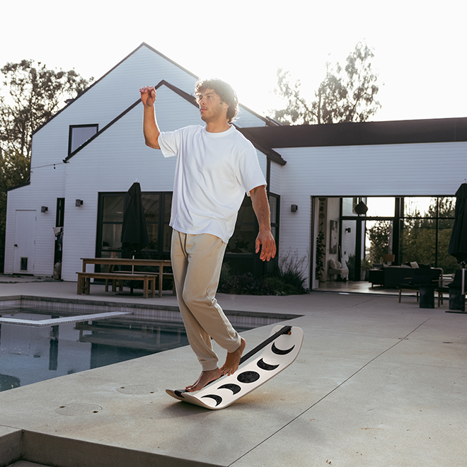 Man balancing on a moon slackboard poolside, with a house in the background