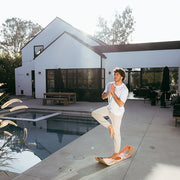 Person practicing yoga on a sunbeam slackboard poolside with a modern house in the background