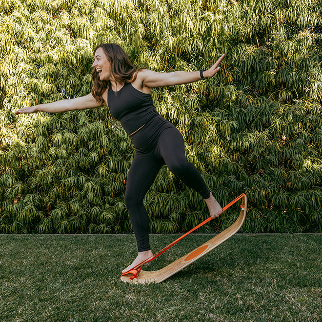 Woman balancing on a sunbeam slackboard plus against a green hedge.