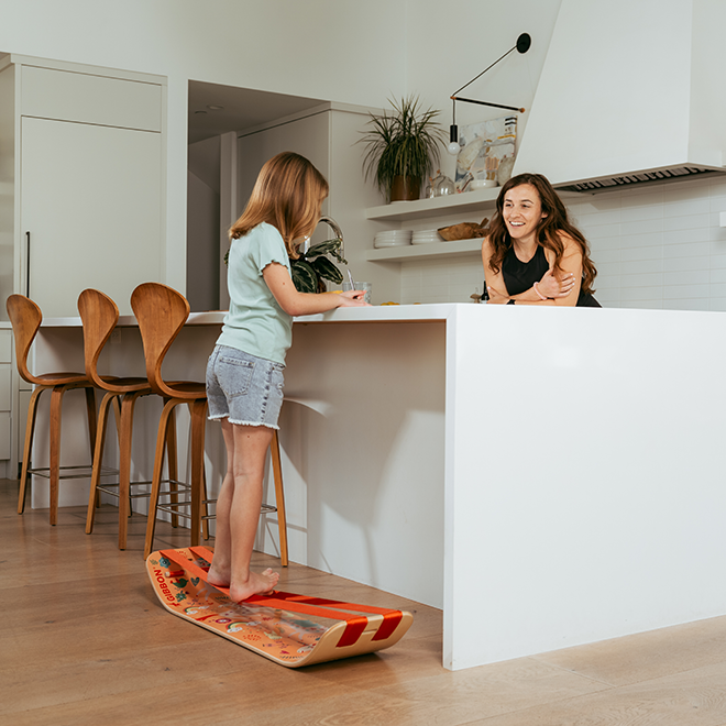 Two women in a modern kitchen with one standing on a wooden unicorn slackboard plus.
